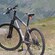 Una mujer parada sobre una roca tomando una foto de una ladera cubierta de hierba con una bicicleta en primer plano